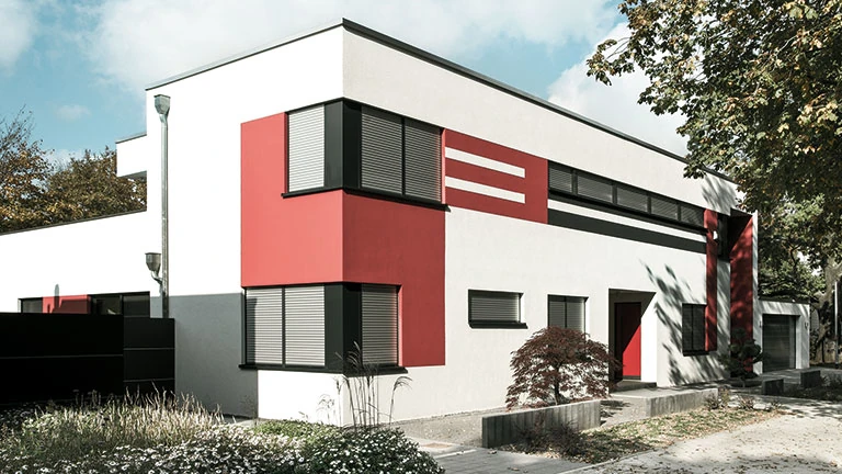 Modernes Einfamilienhaus mit Flachdach, weiß-roter Fassade und Rollläden