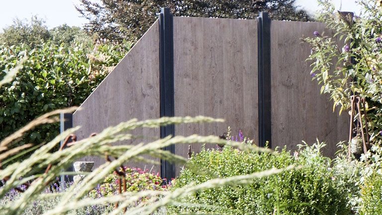 Moderner Sichtschutzzaun aus Holz im Garten, umgeben von Pflanzen und Grün