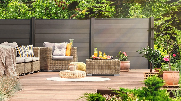 Gartenlounge auf Holzterrasse vor Sichtschutzzaun, Rattanmöbel und Deko